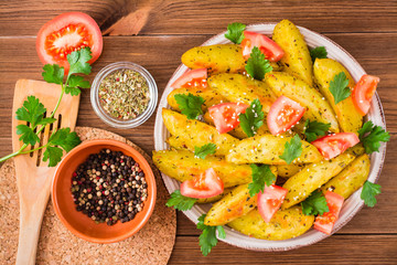 Baked potatoes in a peel with tomatoes, herbs, spices and sesame in a plate. Top View. Wooden table