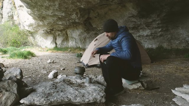 Traveler with smartphone near the tent and heated kettle in the grotto