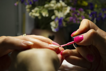 Manicure nail paint. Beautician applying nail polish to female nail in nail salon. Closeup photo