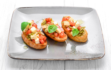 Tasty savory Italian appetizers, or bruschetta, on slices of toasted baguette garnished with basil