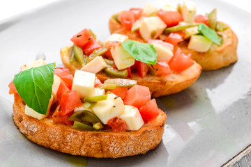Tasty savory Italian appetizers, or bruschetta, on slices of toasted baguette garnished with basil