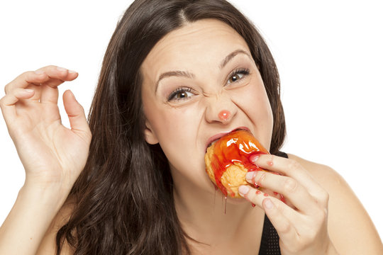 A giddy young woman eats a donut with an topping of cherry on a white background