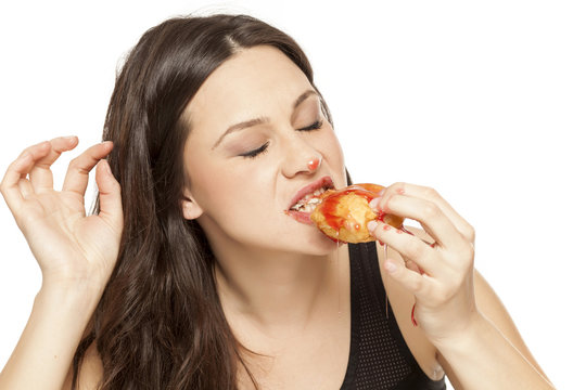 A giddy young woman eats a donut with an topping of cherry on a white background