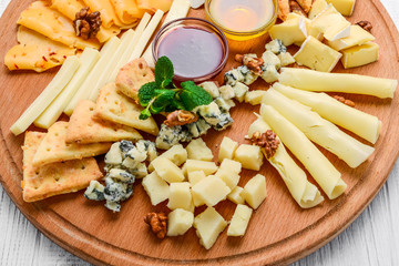 assorted cheese on black slate, nuts and honey, decorated with grapes and mint leaves