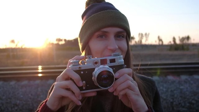 Happy portrait of pretty young beautiful brunette woman hipster photographer taking pictures in outdoor on sunset and smiling. Close up of girl taking photograph with retro camera. Slowmotion.
