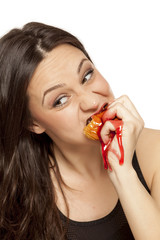 A giddy young woman eats a donut with an topping of cherry on a white background