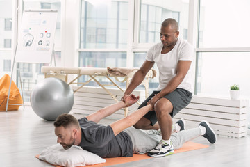 Individual program. Professional nice coach helping his client to perform an exercise while having a special training with him