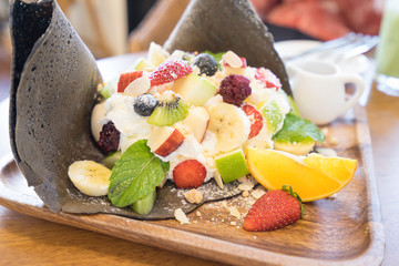 Black crape cake with wipcram topping with fruit berry, banana and orange.