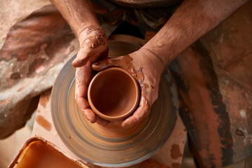 Close-up hands of a male potter in apron making a vase from clay, selective focus