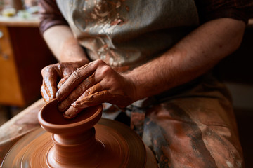 Close-up hands of a male potter in apron making a vase from clay, selective focus