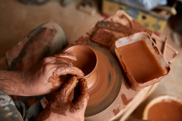 Close-up hands of a male potter in apron making a vase from clay, selective focus