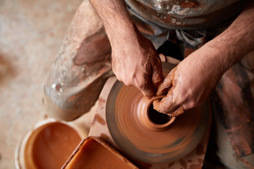 Close-up hands of a male potter in apron making a vase from clay, selective focus