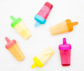 A flat lay of colourful, frozen, fruit smoothie iced lollies on a white background