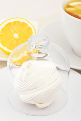 A cup of tea with lemon slices and zephyr, which is covered with a glass cap. Selective focus.