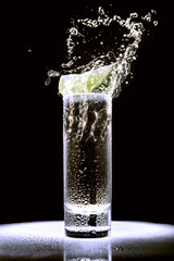 a glass of tequila with a piece of lime on a black background