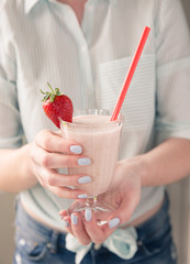 A midsection of a fashionable young girl in pastel colours holding a pink glass of strawberry milkshake or smoothie decorated with fruit and a straw