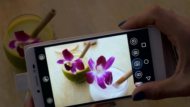The girl takes pictures of beautiful cocktails with flowers on a smartphone.