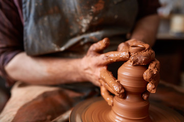 Close-up hands of a male potter in apron making a vase from clay, selective focus