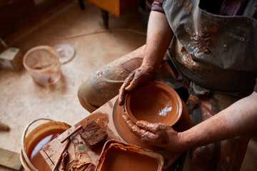 Close-up hands of a male potter in apron making a vase from clay, selective focus