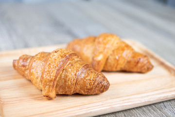 Two croissant are placed on a wooden chopping board and gray table