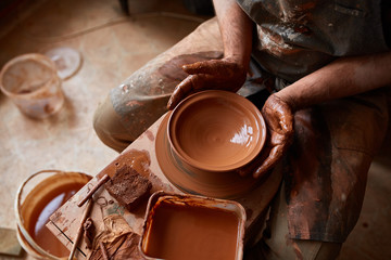 Portrait of a male potter in apron molds bowl from clay, selective focus, close-up