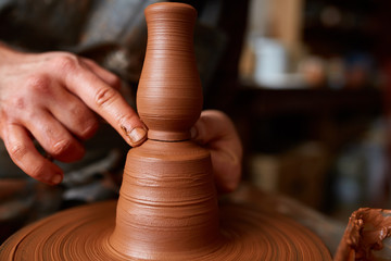 Close-up hands of a male potter in apron making a vase from clay, selective focus