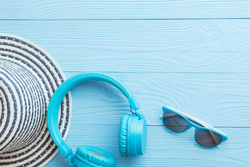 Flat lay of modern big headphones, hat and sunglasses of blue colors composed on blue wood.