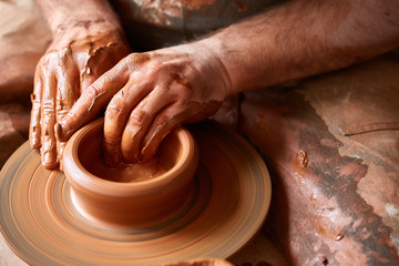 Close-up hands of a male potter in apron making a vase from clay, selective focus