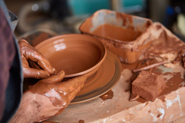 Close-up hands of a male potter in apron making a vase from clay, selective focus