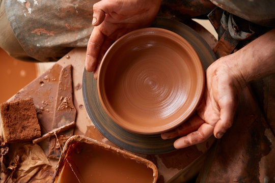 Close-up hands of a male potter in apron making a vase from clay, selective focus