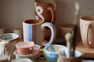 Close-up of various paint mugs and brushes in holder on worktop, selective focus, side view.