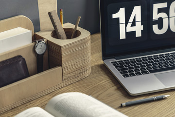 Close-up of wooden desk organizer with pencil and watch, computer, pen and book lying on the desk