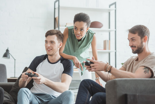 young african american woman watching two men playing video game with joysticks in hands