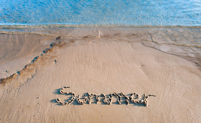The word summer is written in the sand. The inscription is made by hand. Blue sea wave.