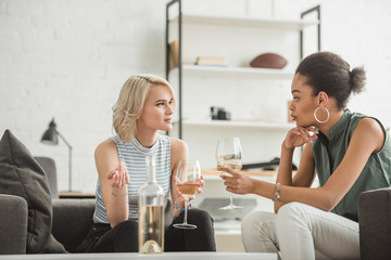 Obraz na płótnie Canvas multiethnic young women sitting and talking with glasses of white wine