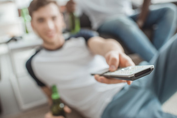 closeup shot of remote in hand of man sitting with bottle of beer