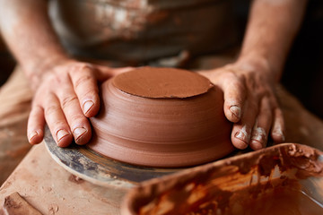 Close-up hands of a male potter in apron making a vase from clay, selective focus