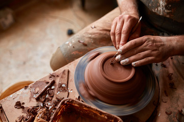 Close-up hands of a male potter in apron making a vase from clay, selective focus