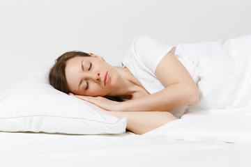 Calm young brunette woman lying in bed with white sheet, pillow, blanket on white background. Sleeping beauty female spending time in room. Rest, relax, good mood concept. Copy space for advertisement