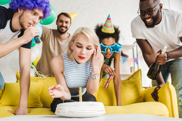Blonde woman blowing candle on birthday cake by her cheerful friends