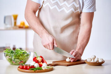 Man cooking at kitchen making healthy vegetable salad, close-up, selective focus.