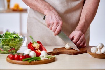 Man cooking at kitchen making healthy vegetable salad, close-up, selective focus.