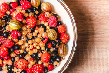 Fruit salad with strawberry, raspberries, gooseberry, currant, sweet on wooden white background. Flat lay, top view. Vitamins healthy eating