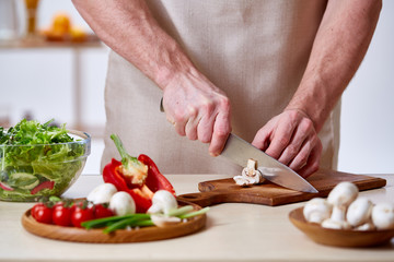 Man cooking at kitchen making healthy vegetable salad, close-up, selective focus.