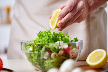 Man cooking at kitchen making healthy vegetable salad, close-up, selective focus.
