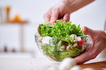 Man cooking at kitchen making healthy vegetable salad, close-up, selective focus.