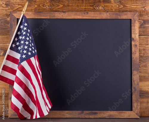 Blank blackboard next to American flag on a wooden background