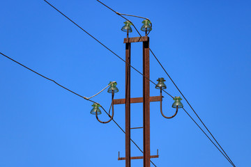Rusty metal power line support with wires and glass insulators close-up against the blue sky