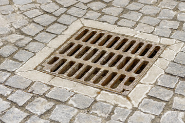sewer grate for rainwater installed near the road and surrounded by cobblestones