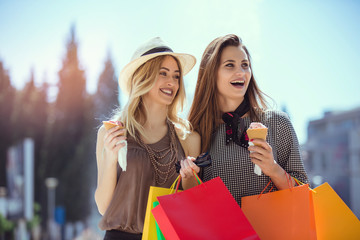 Happy young women with shopping bags and ice cream having fun on city street